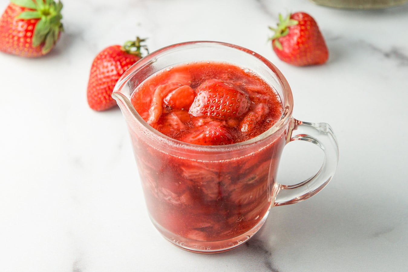 A small glass jar filled with strawberry sauce with strawberries on the table