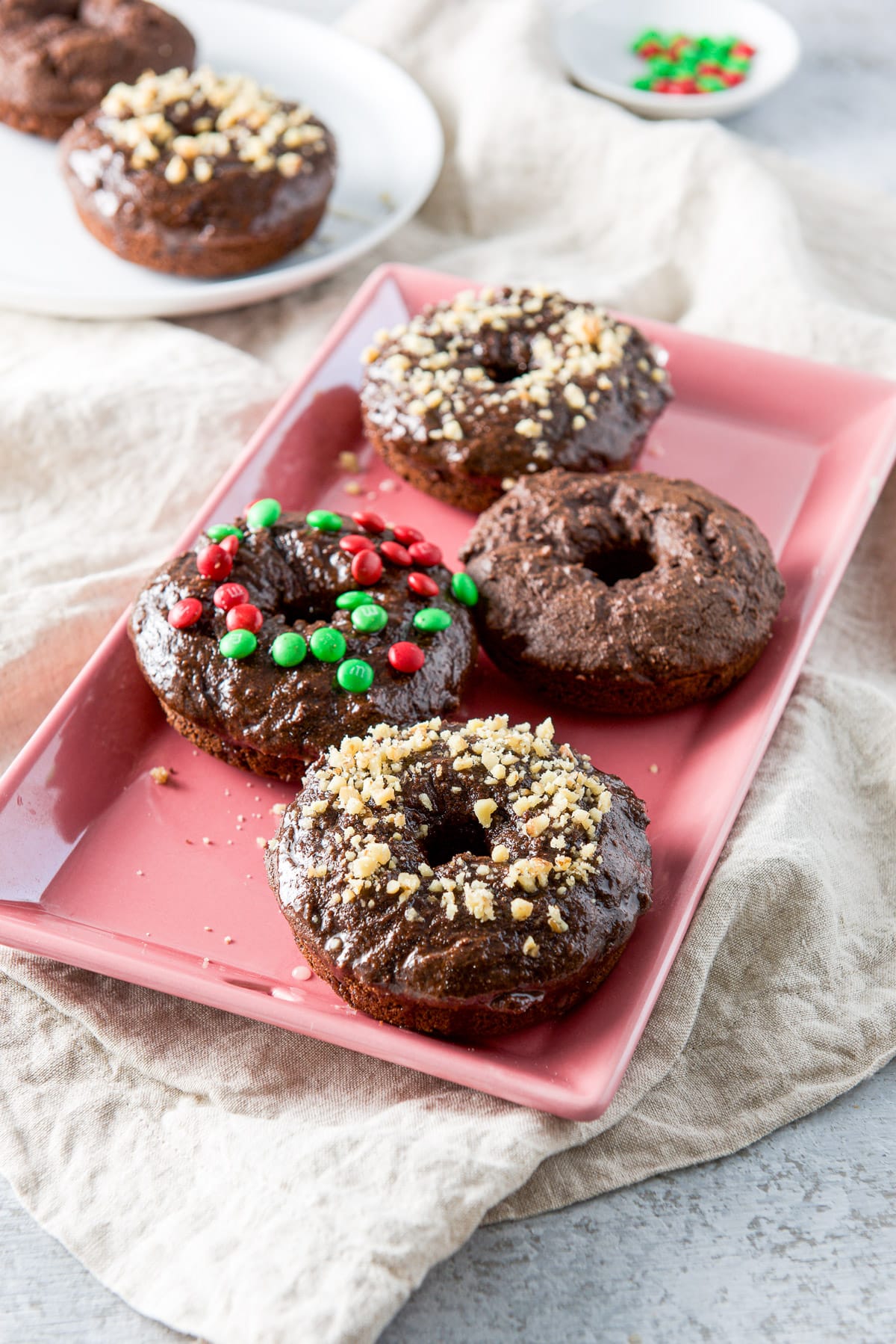 A pink platter with four decorated donuts on it, with a plate in the back