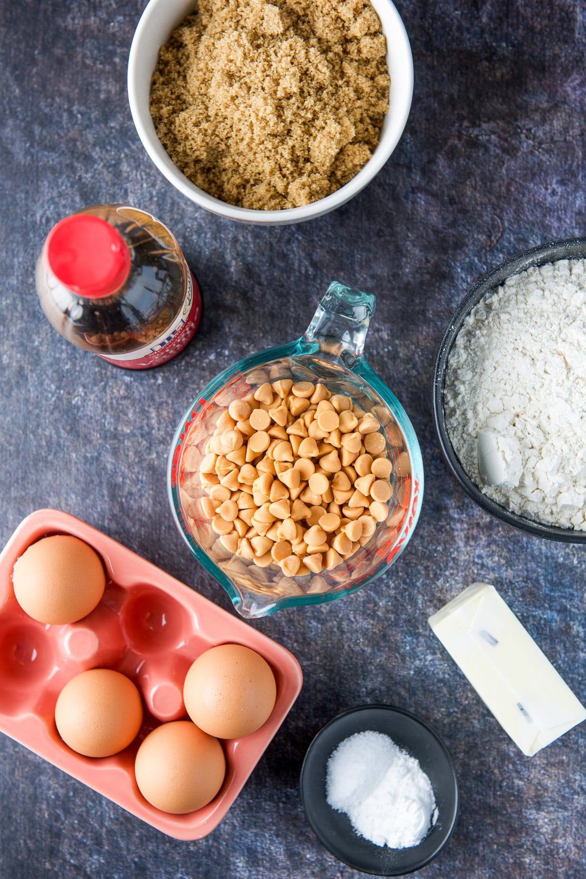 Overhead view of eggs, flour, sugar, butterscotch chips, butter, leavening agents, and vanilla