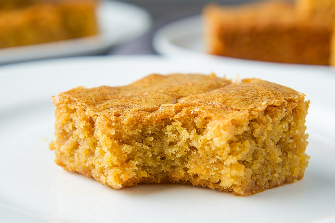 A horizontal photo of a blonde brownie with a bite taken out of it - on a white plate