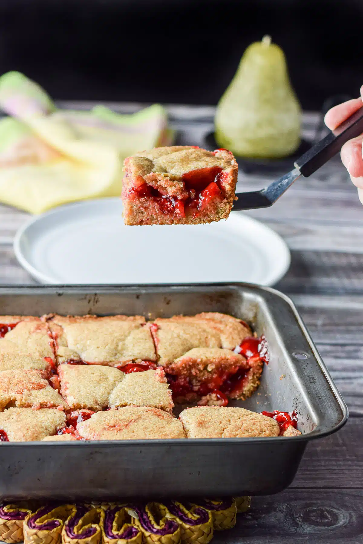 A hand holding a spatula with a piece of the cherry dessert held over the pan