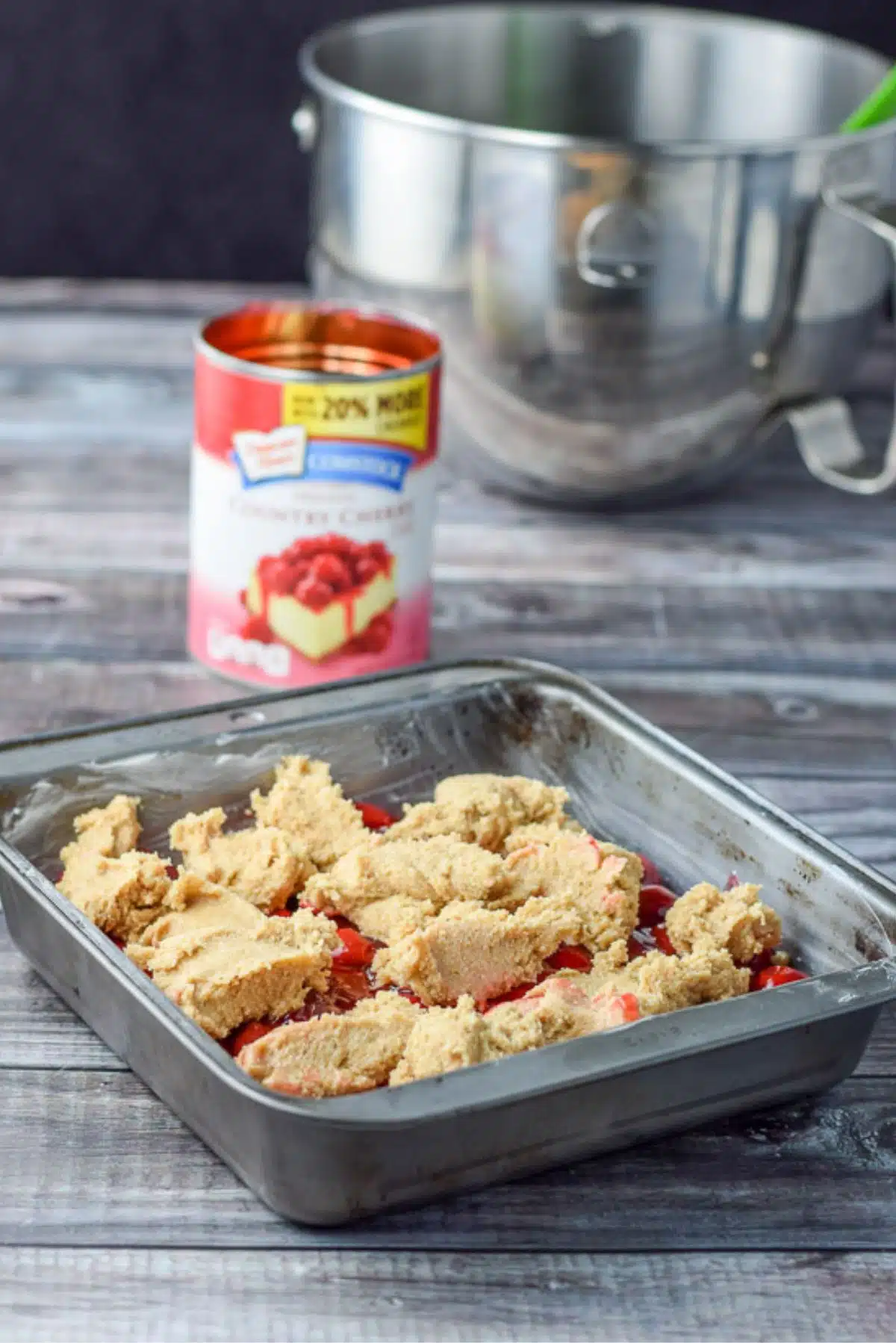 Batter dropped on top of the cherry filling along with the mixing bowl and cherries in the background