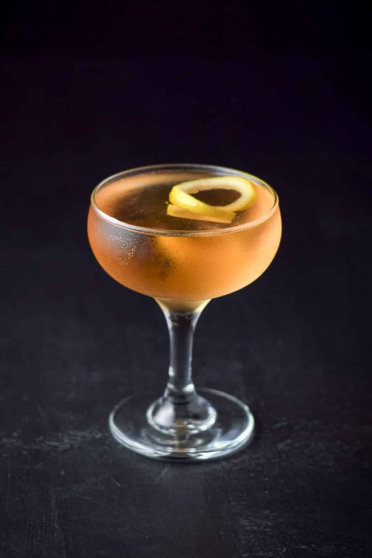 A coupe glass with an amber the el presidente and a lemon twist in it