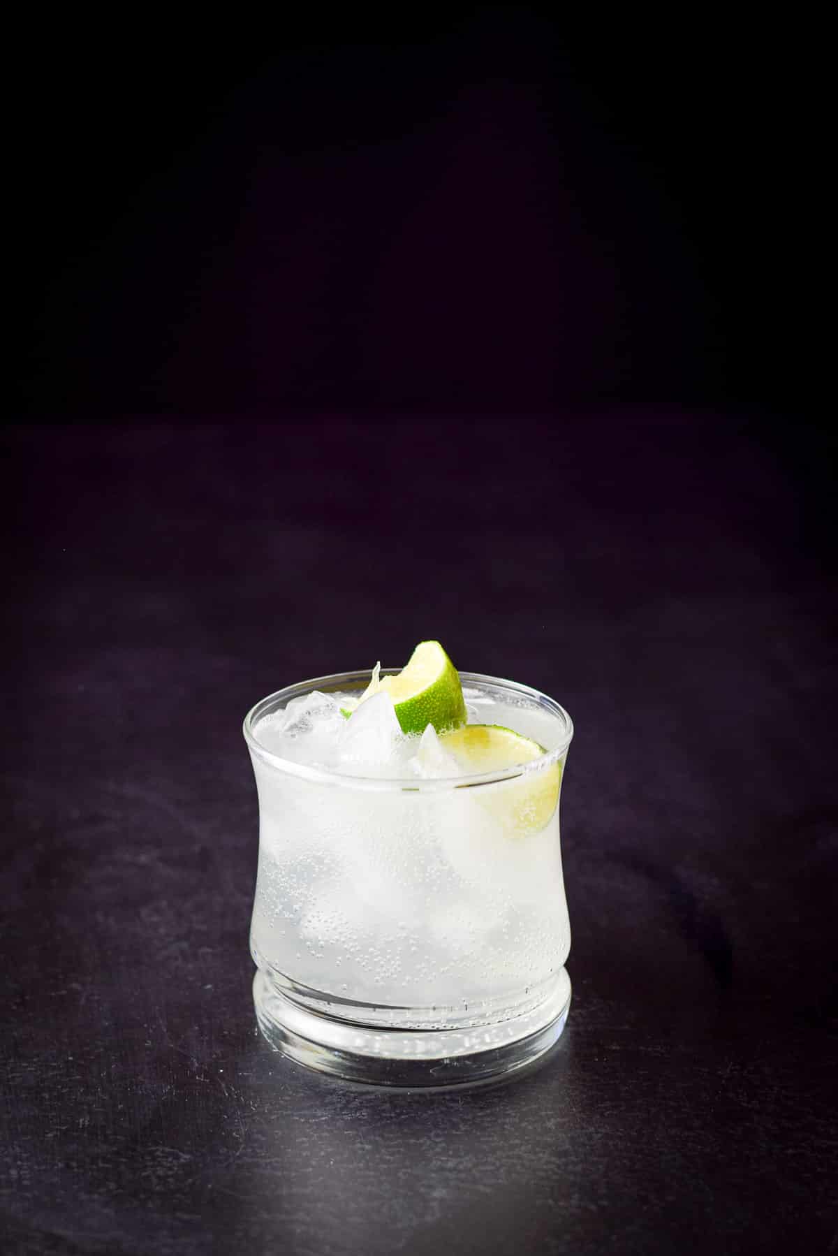 Dark shot of a double old fashioned glass filled with the cocktail with two lime wedges in it