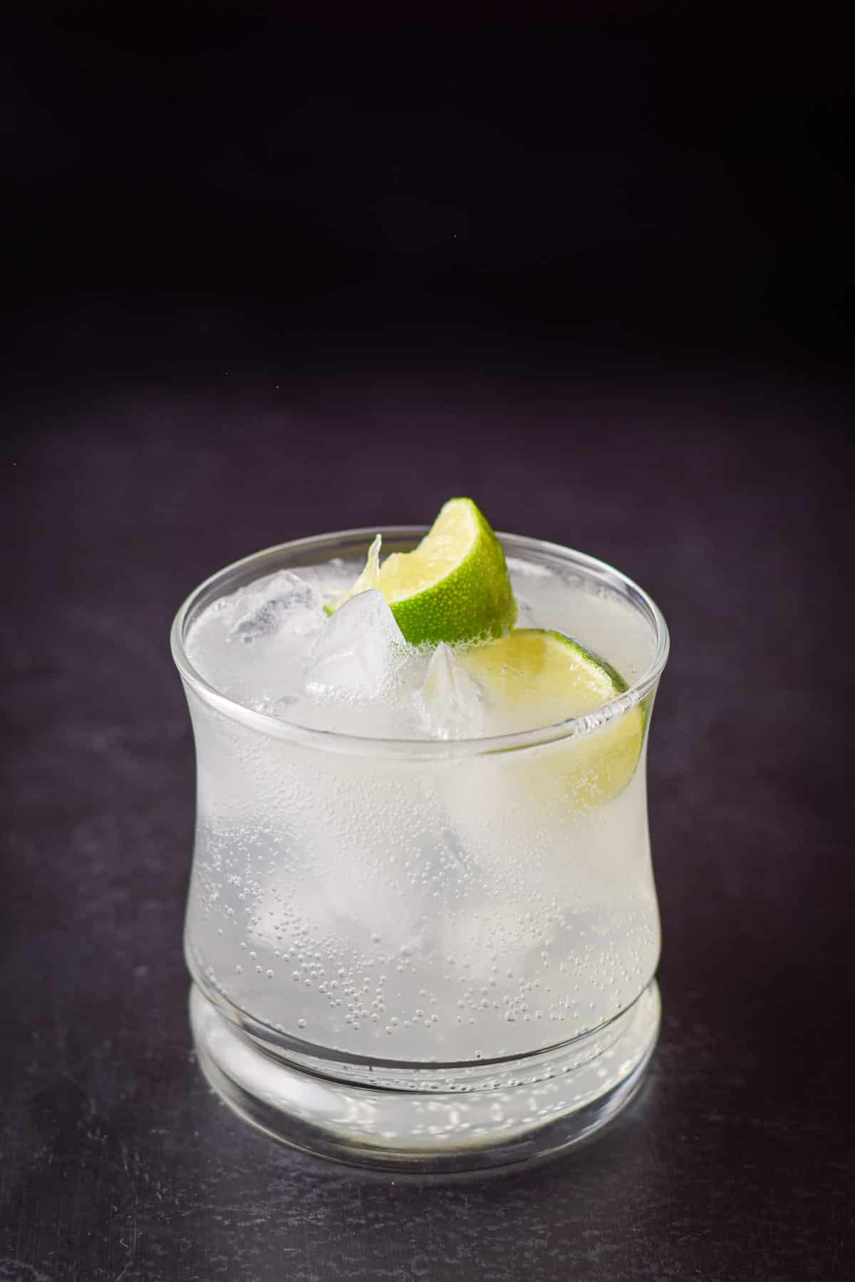 A close view of the cocktail and two lime wedges in a double old fashioned glass