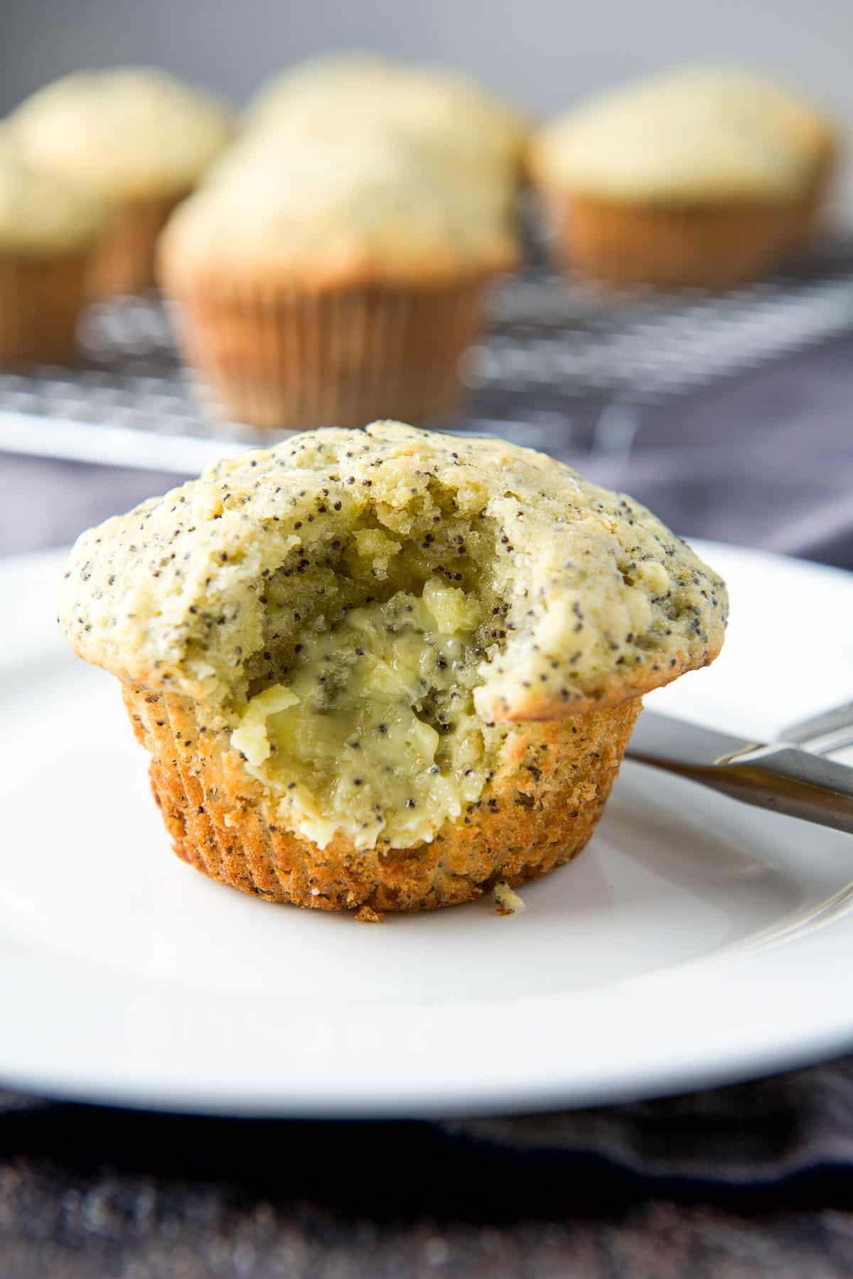 Close up of a muffin with a bite taken out of it on a white plate and butter slathered in that bite