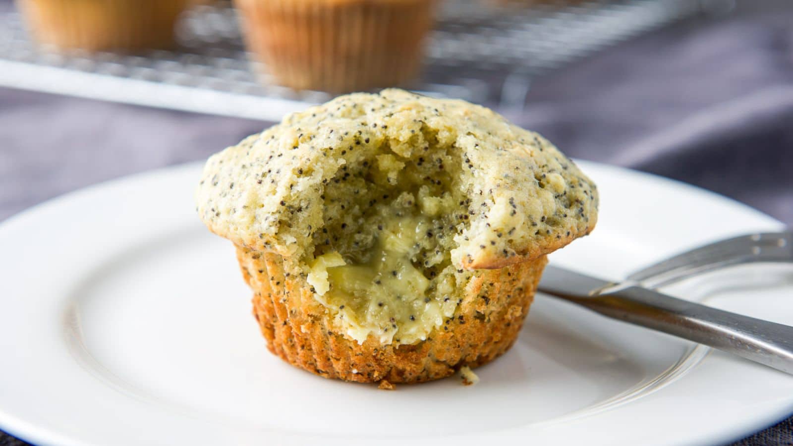 Close-up of a muffin with a bite taken out of it on a white plate and butter slathered in that bite