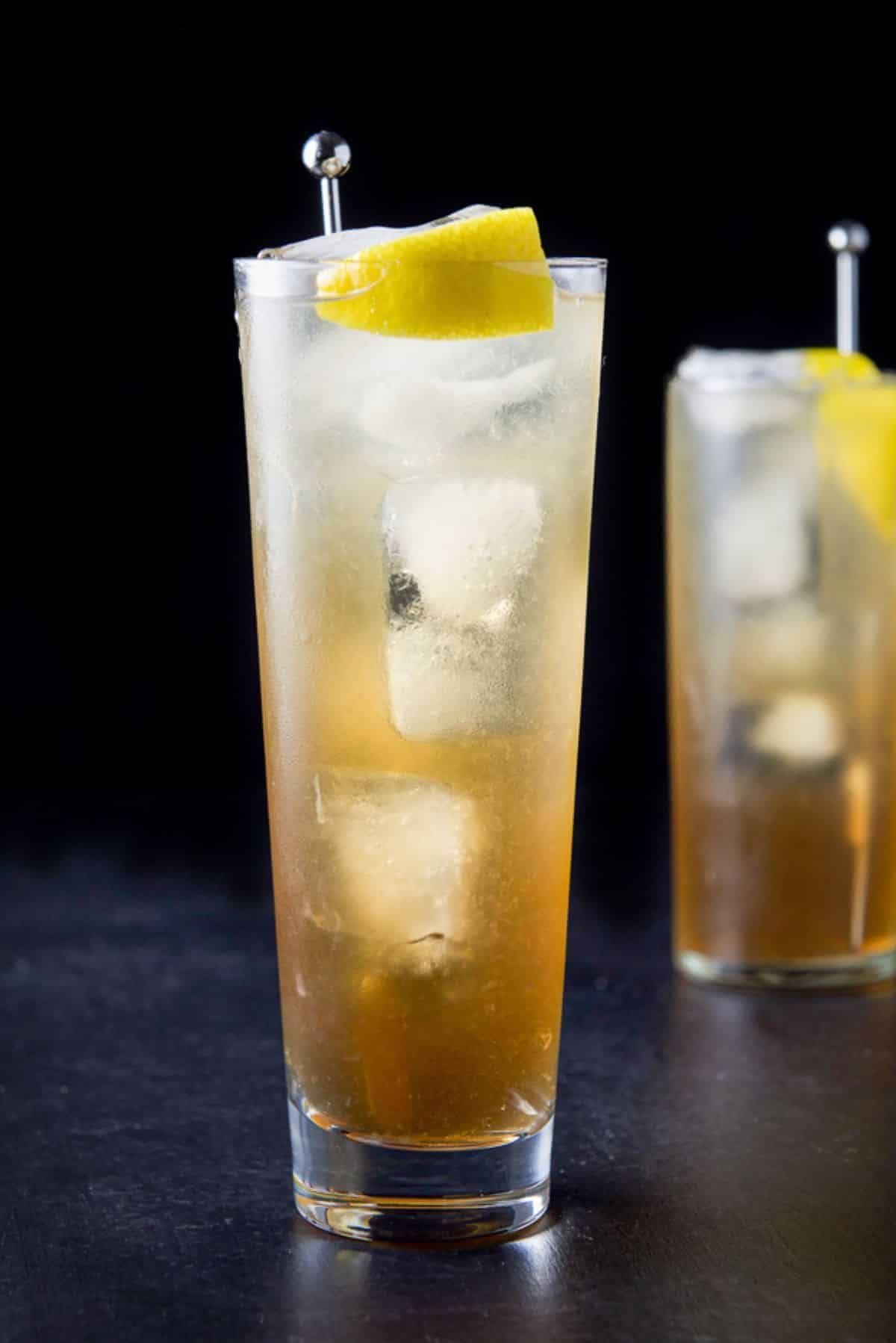 Vertical view of the wider glass filled with the potent cocktail with a lemon wedge and stirrer