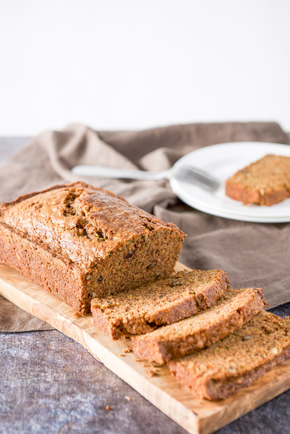 The quick bread cut into slices on a wooden board with a piece on a plate in the background