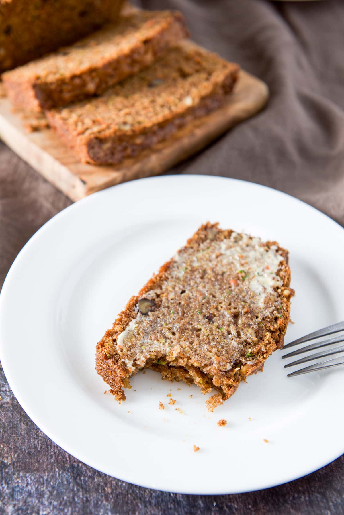 A bite taken out of the zucchini bread on a white plate with some slices in the background