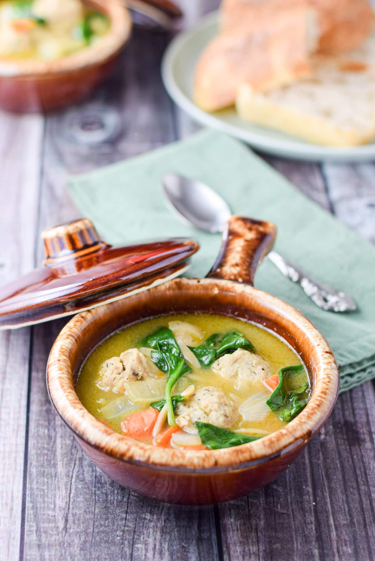 Two brown crocks filled with the meatball soup with a plate of bread in the background