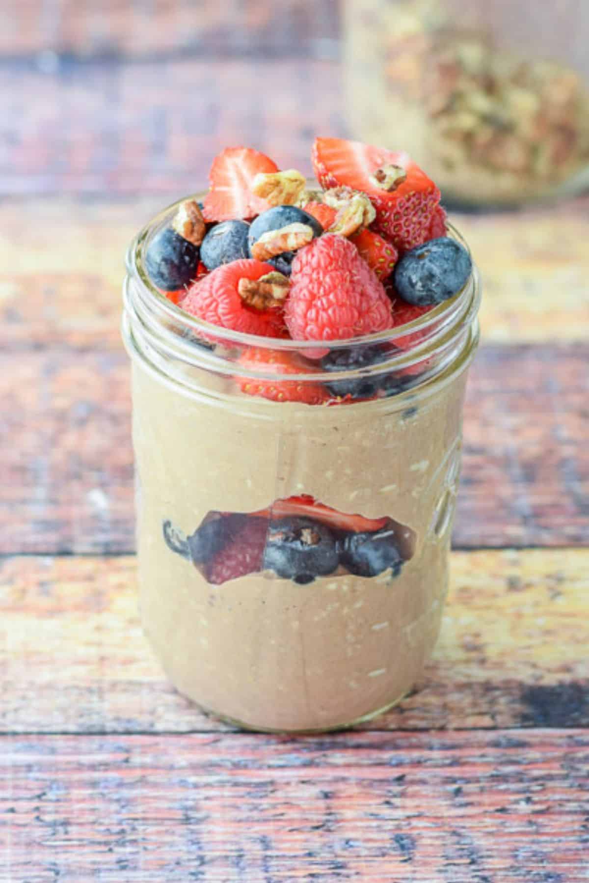 A jar with chocolate oats with fruit between the two layers and on top with walnuts