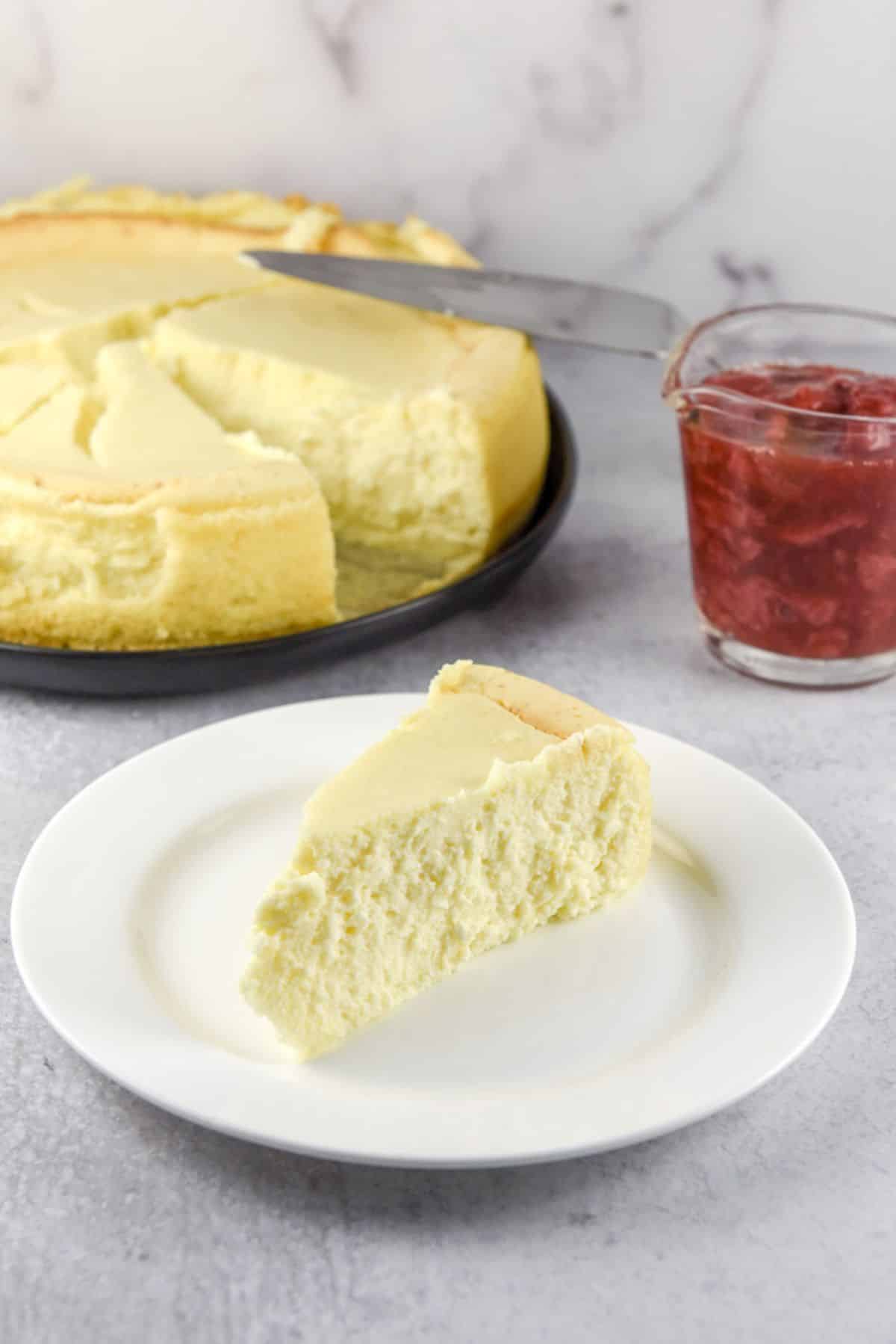 Plain slice of cheesecake on a plate with strawberries made into a sauce behind it