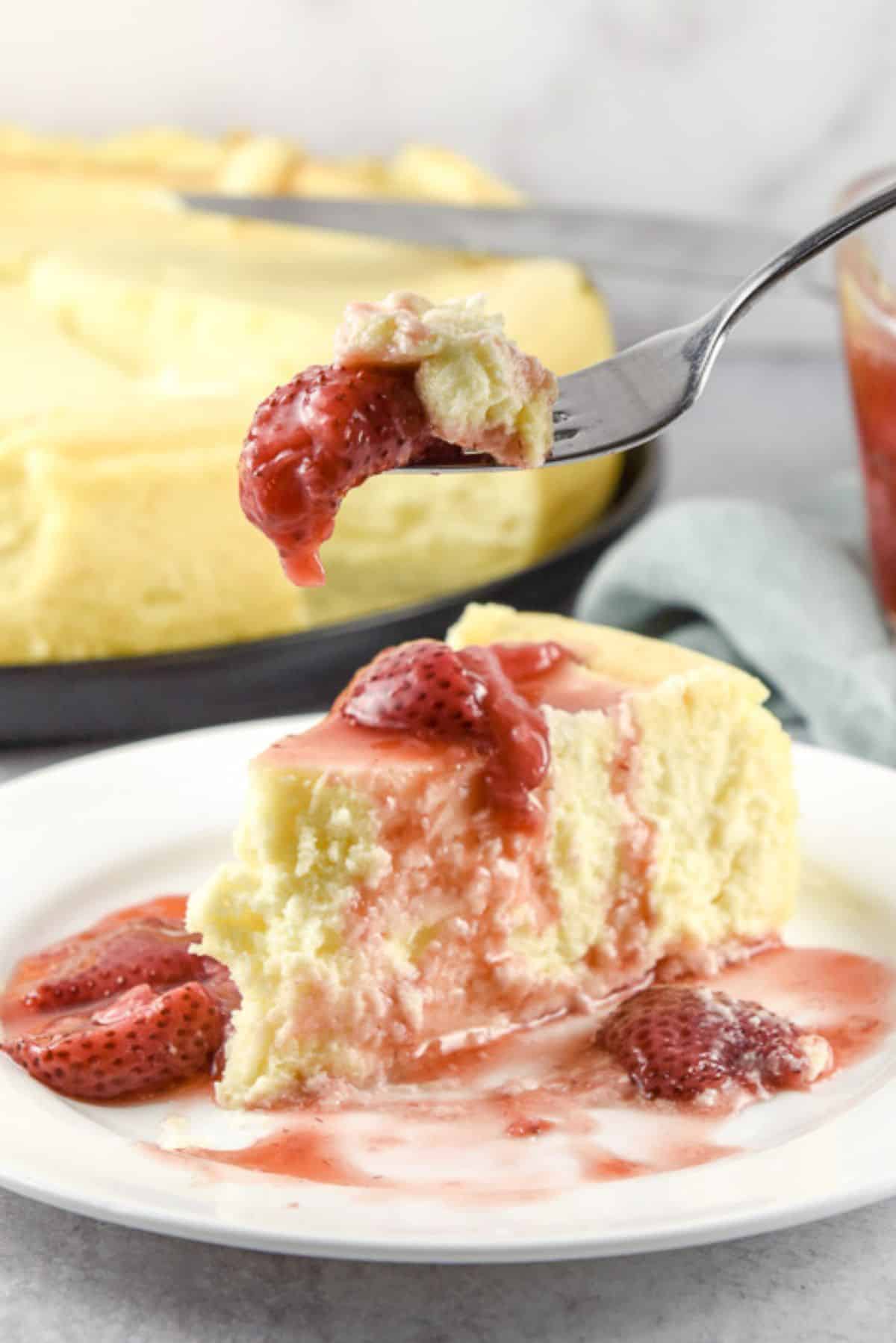 A forkful of cheesecake with a strawberry held over the piece of cheesecake