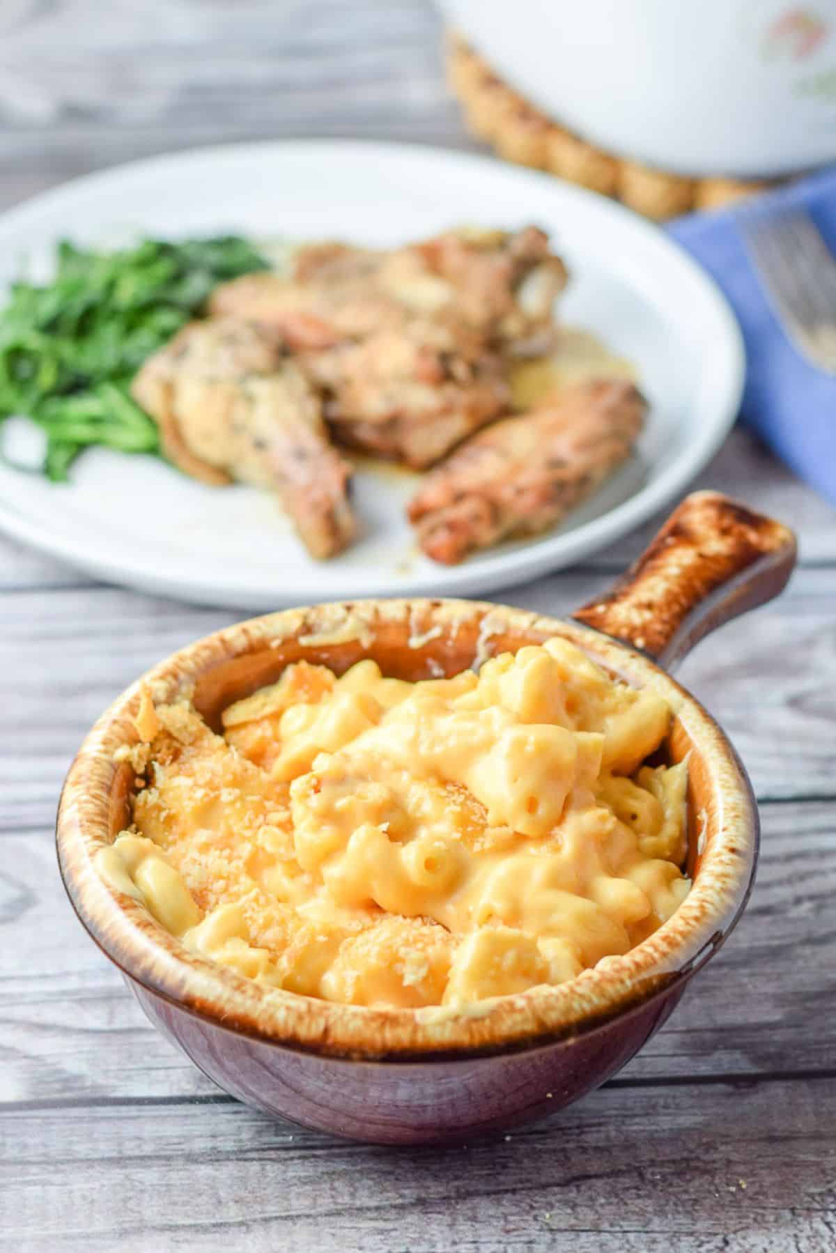 A plate of food behind a brown crock of mac and cheese