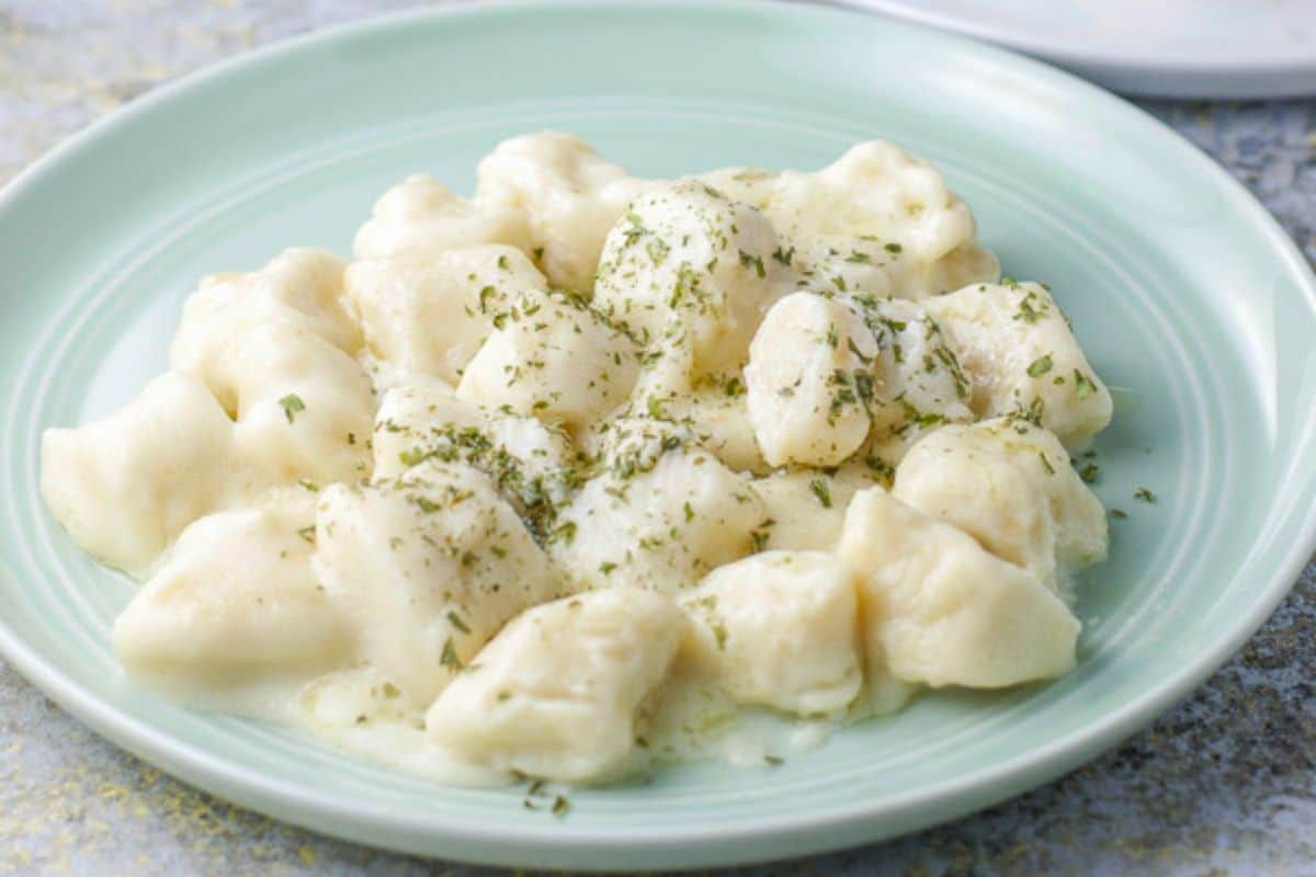 A green plate with gnocchi, cheese sauce, and herbs on top