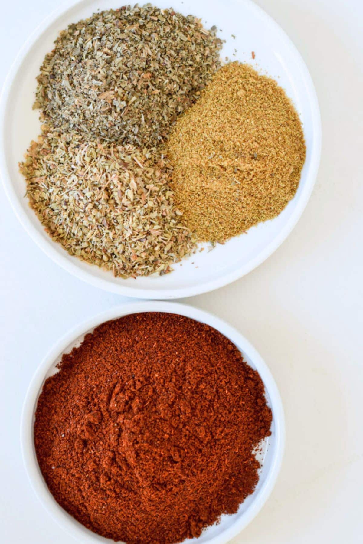Chili powder, cumin, basil and oregano in small white dishes