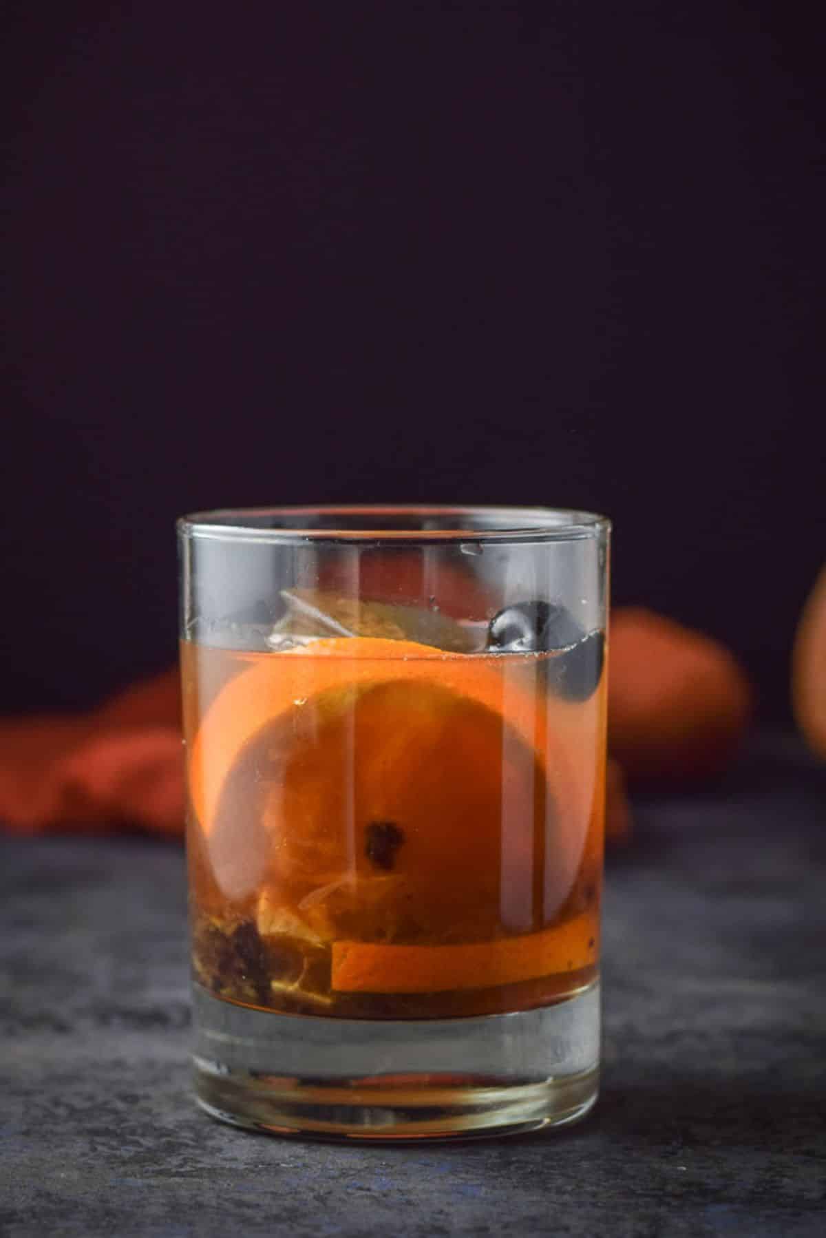 Vertical view of the glass with the cocktail in it with a orange slice and cherry for garnish