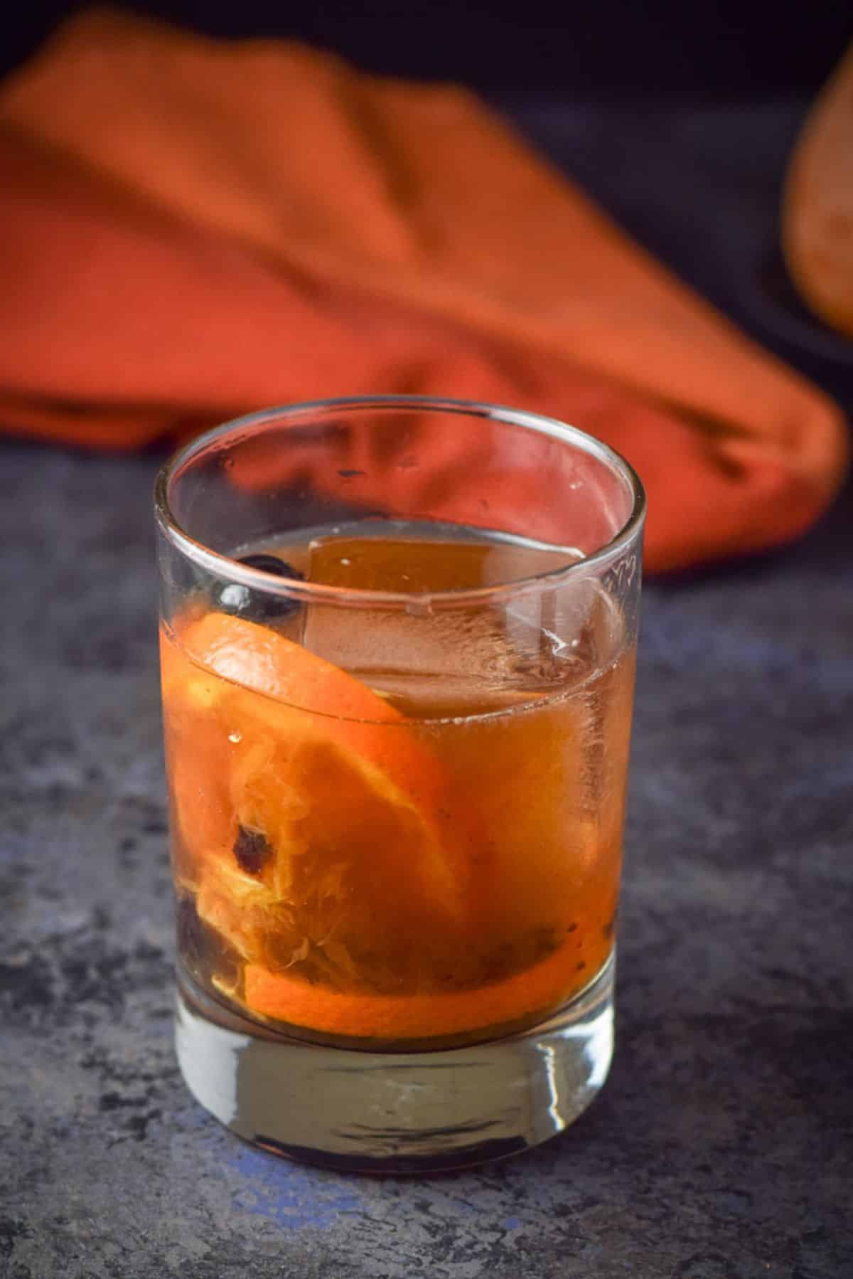 A double old fashioned glass with the cocktail in it along with cherry and orange as garnish