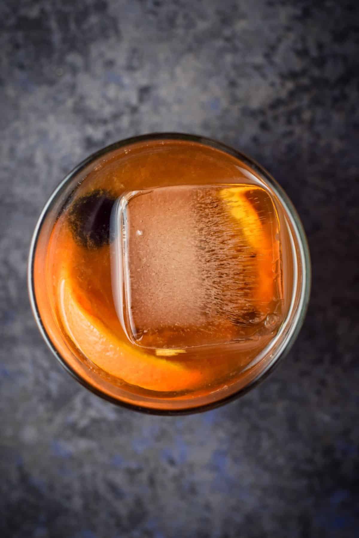 Overhead view of a big cube in the cocktail with a cherry and orange slice