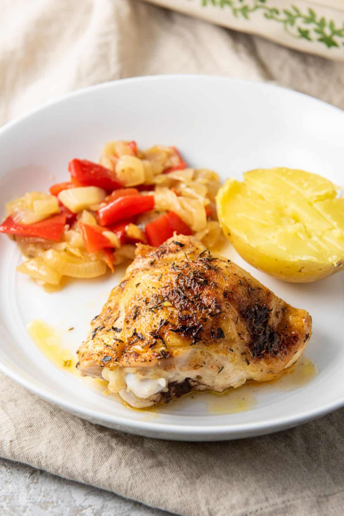 chicken thighs on a plate with vegetables and a potato