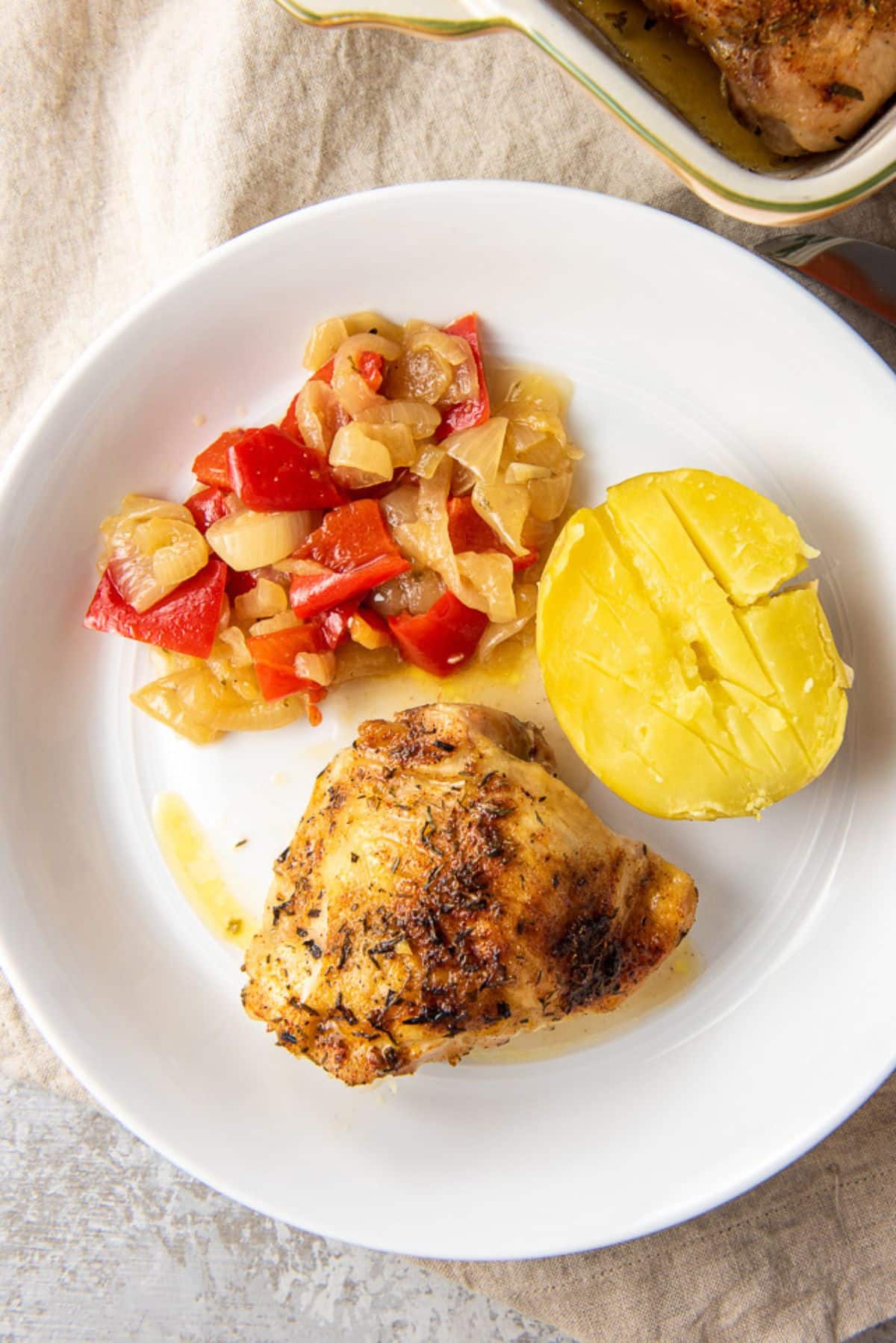 Overhead view of the of a chicken thigh on a plate with veggies and the baking dish off to the side