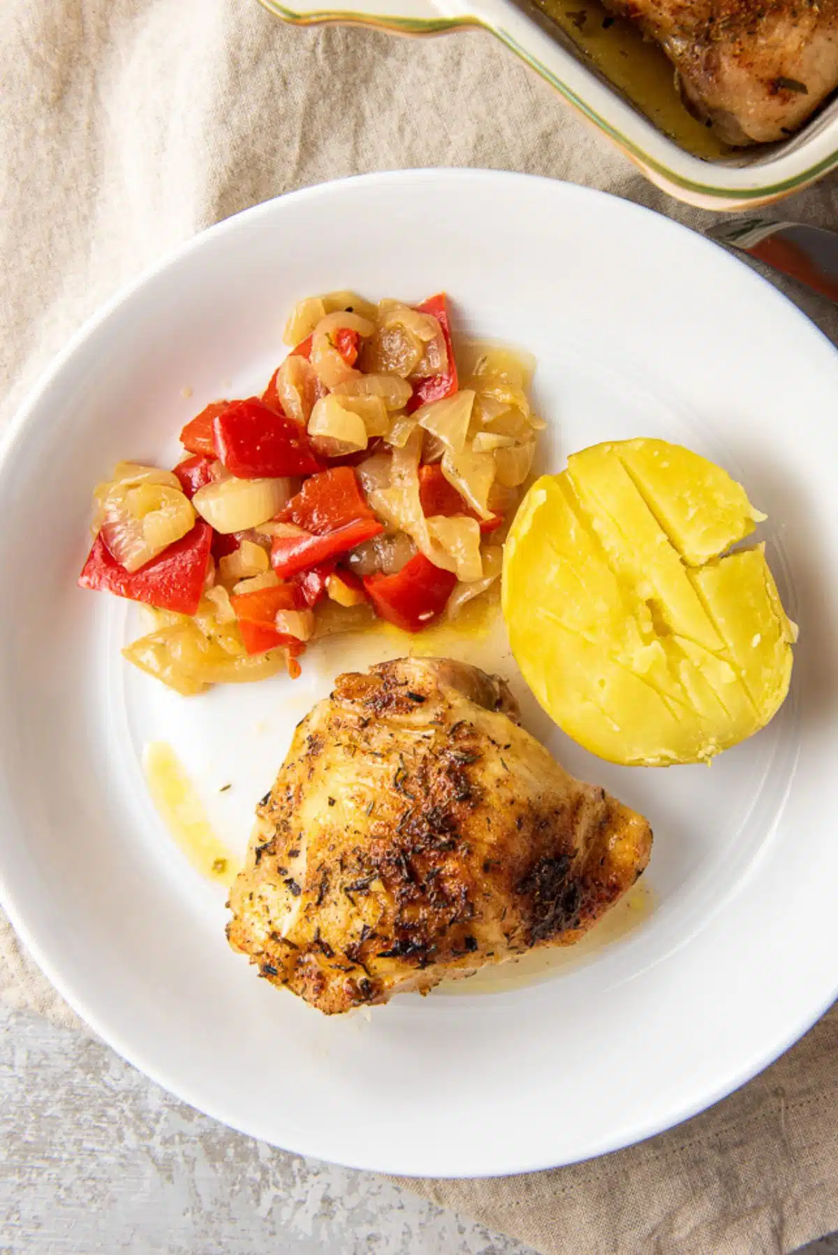 Overhead view of the of a chicken thigh on a plate with veggies and the baking dish off to the side