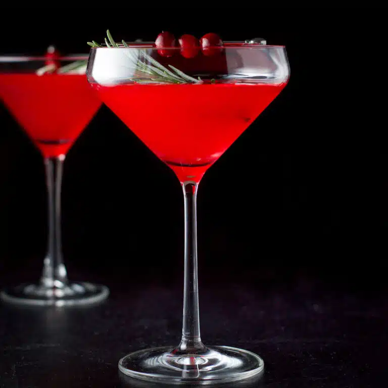 a square photo of two glasses filled with a cranberry cosmo, with cranberries and rosemary for garnish