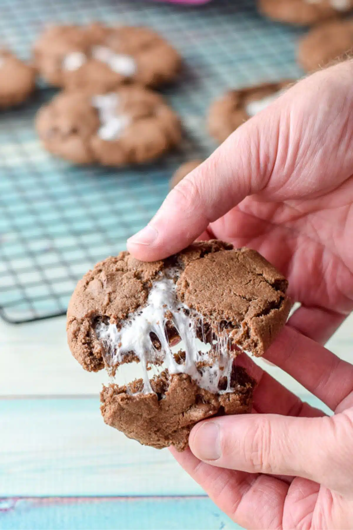 A male hand pulling apart a chocolate marshmallow cookie with more in the background