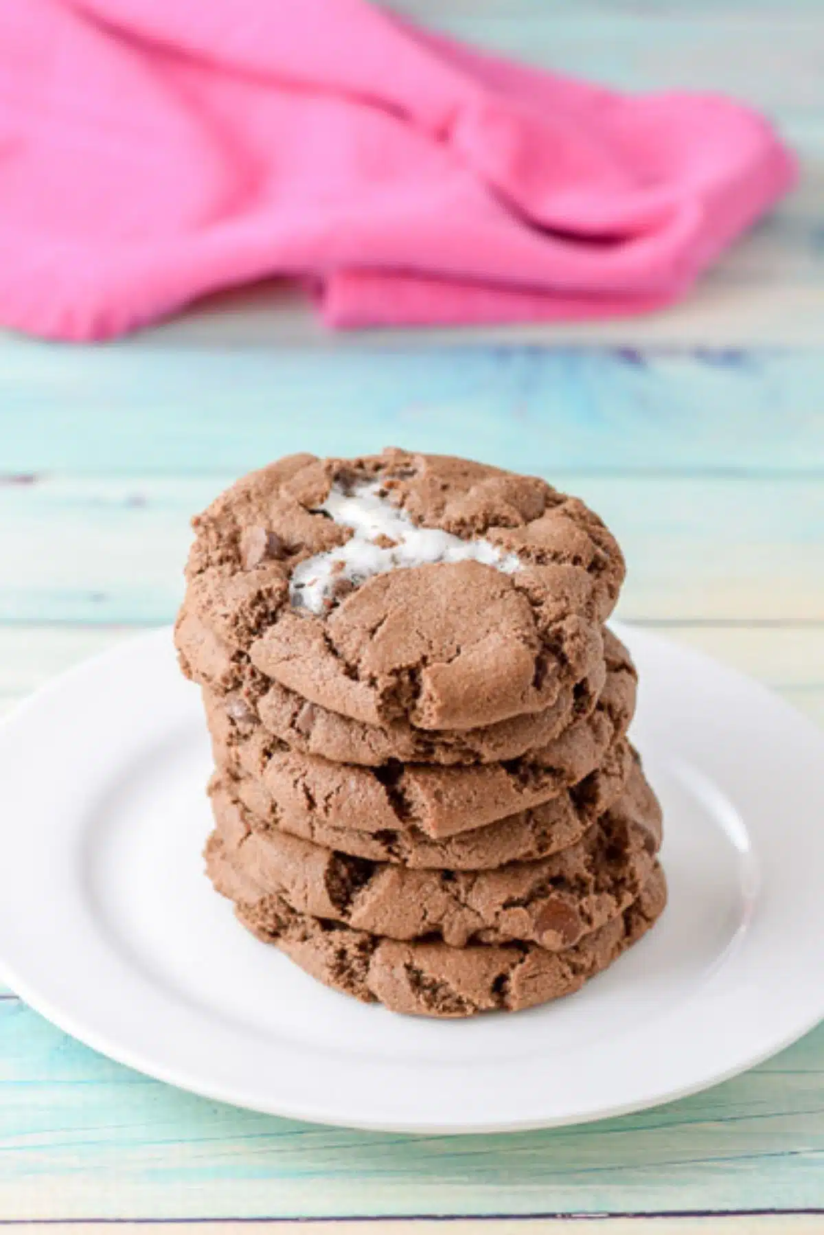 A white plate with a pile of chocolate cookies with marshallow baked in it on a greenish table