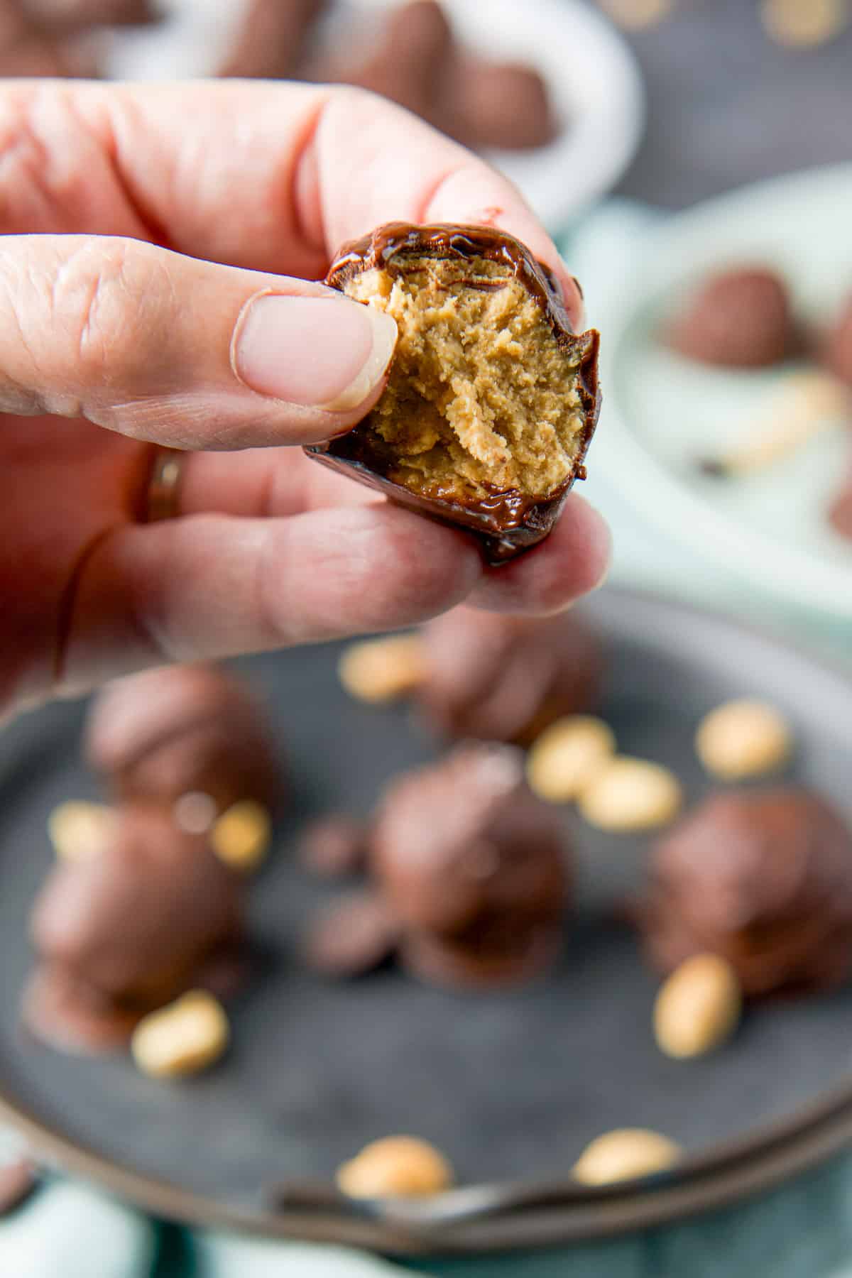 A female hand holding a peanut butter ball with a bite taken out of it