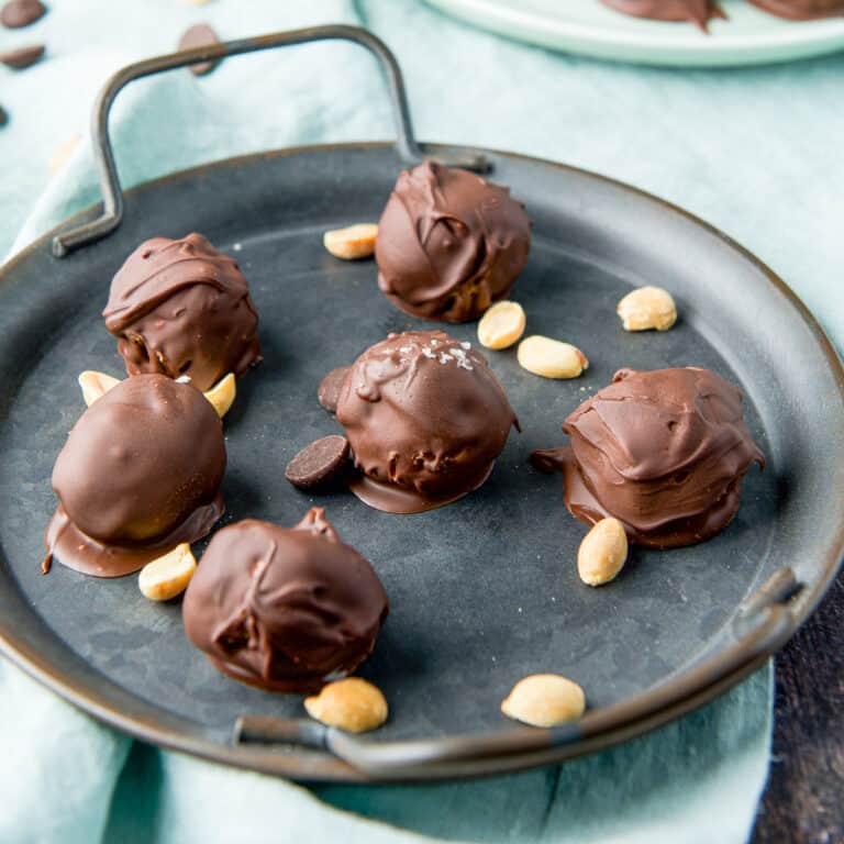 A metal tray with chocolate peanut butter balls and peanuts on it as well