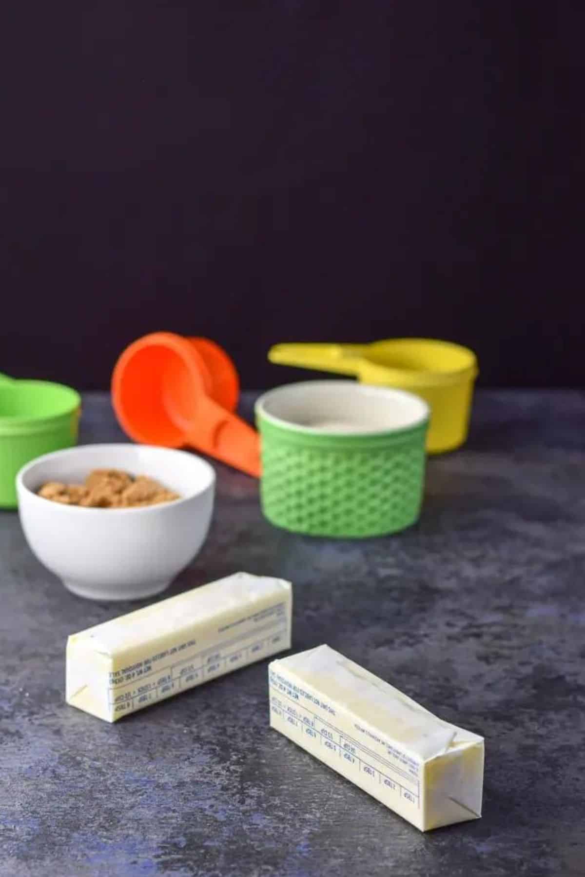 Butter, brown sugar and cane sugar on a table with colorful measuring cups