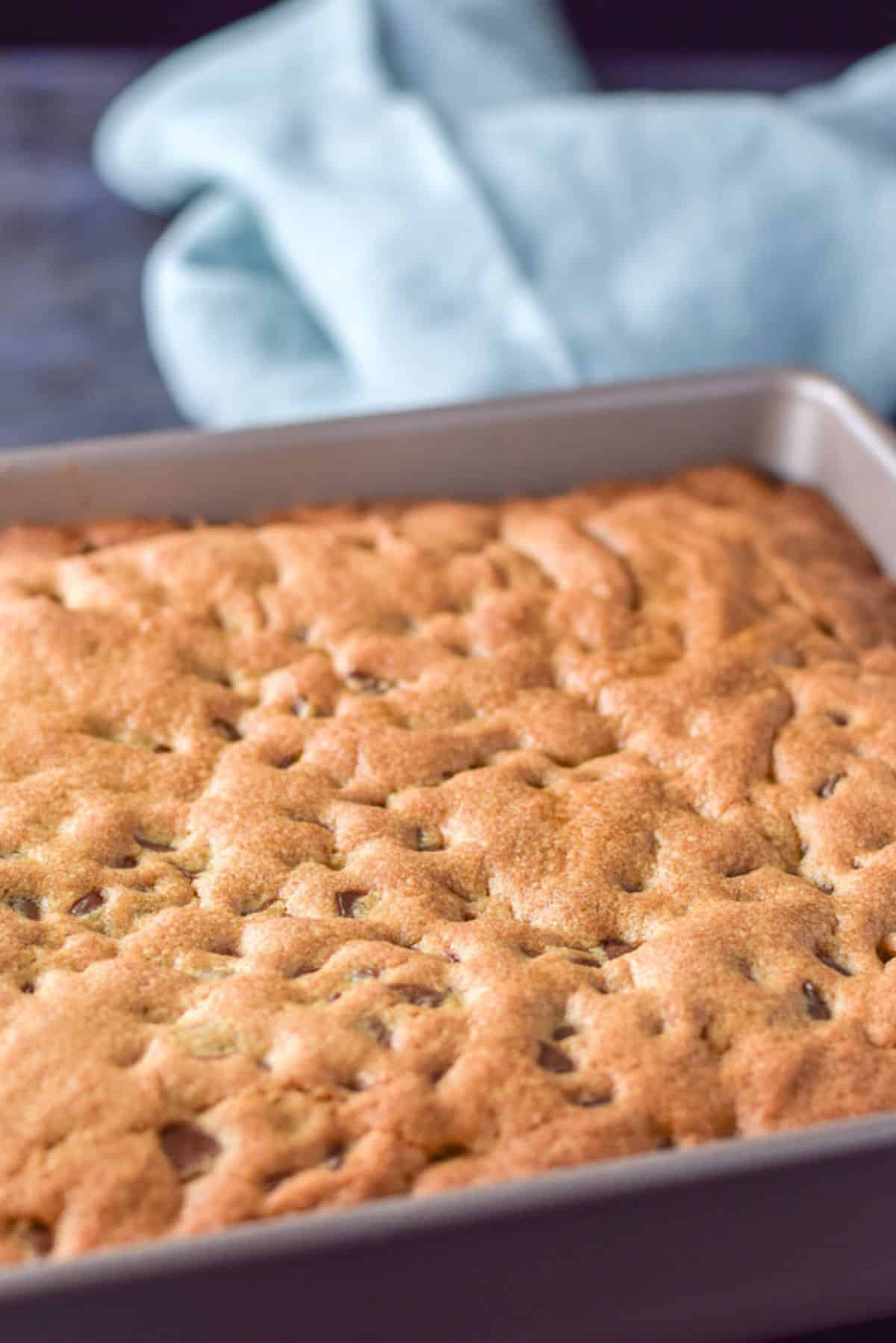 Close up of a pan of chocolate chip squares fresh out of the oven and a napkin in the background