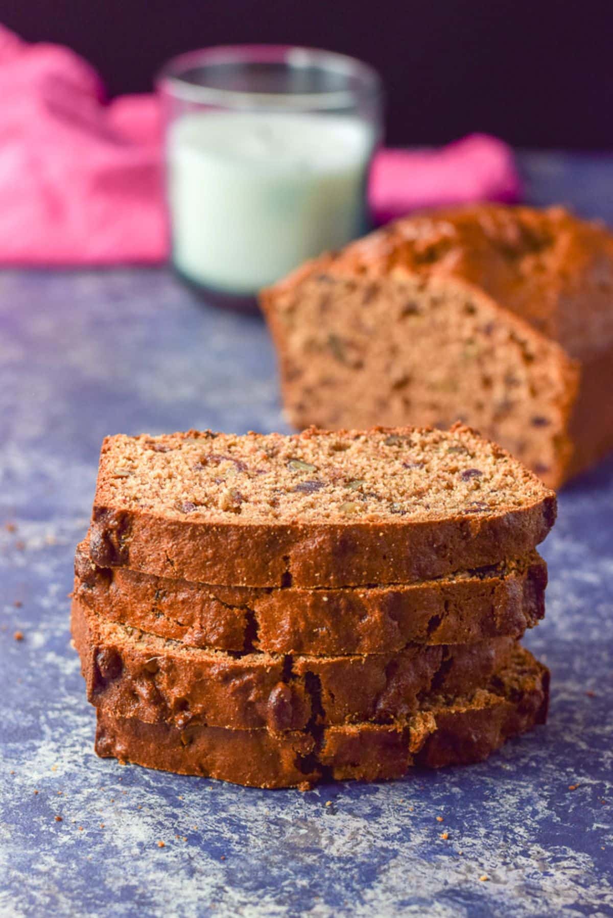 Four slices of bread stacked on each other with the loaf behind it and a candle and napkin