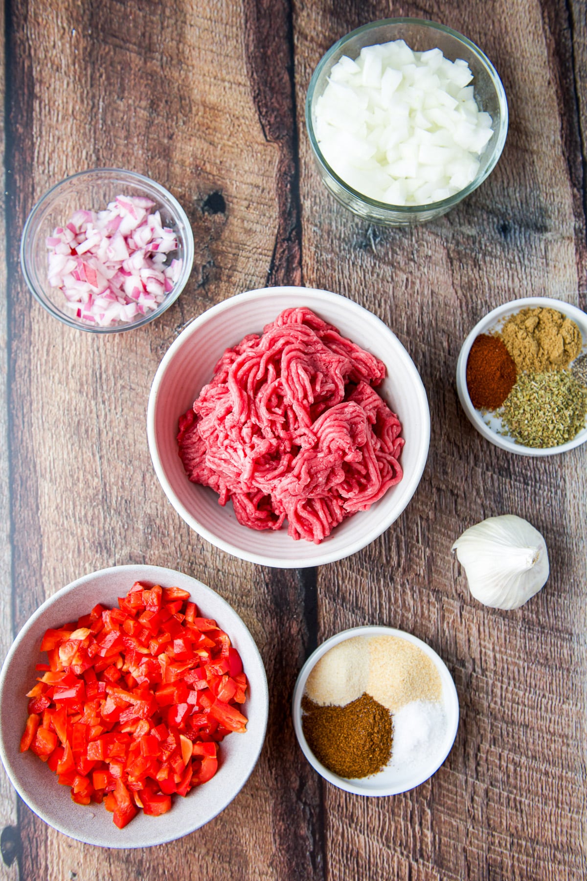 Overhead view of ground beef, diced onions, diced bell pepper, herbs, spices, and garlic