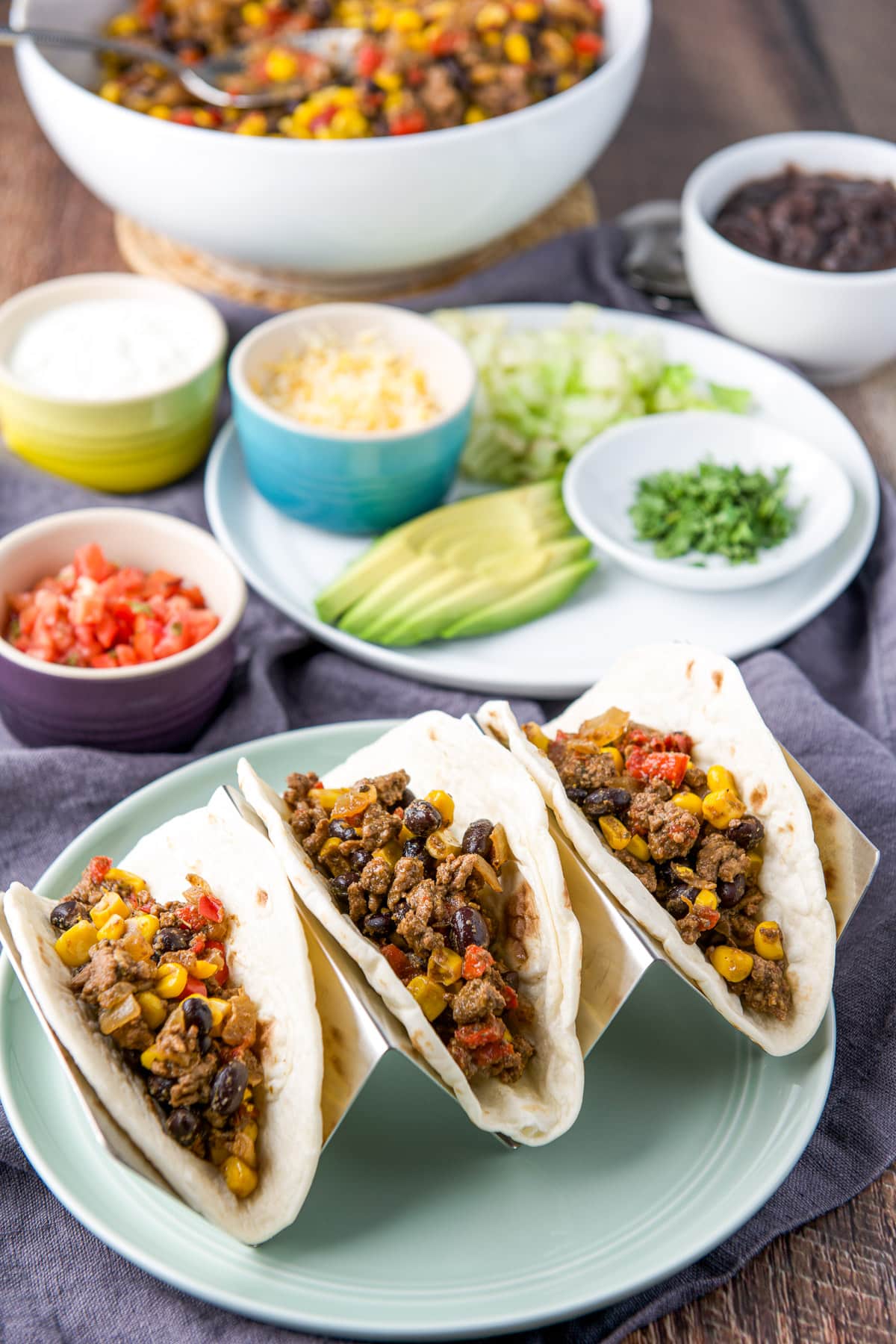 Three tacos with the ground beef mixture in them with all the fixings in the back