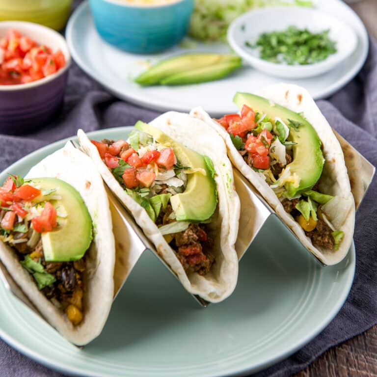 square photo of three tacos in a holder with all the fixings
