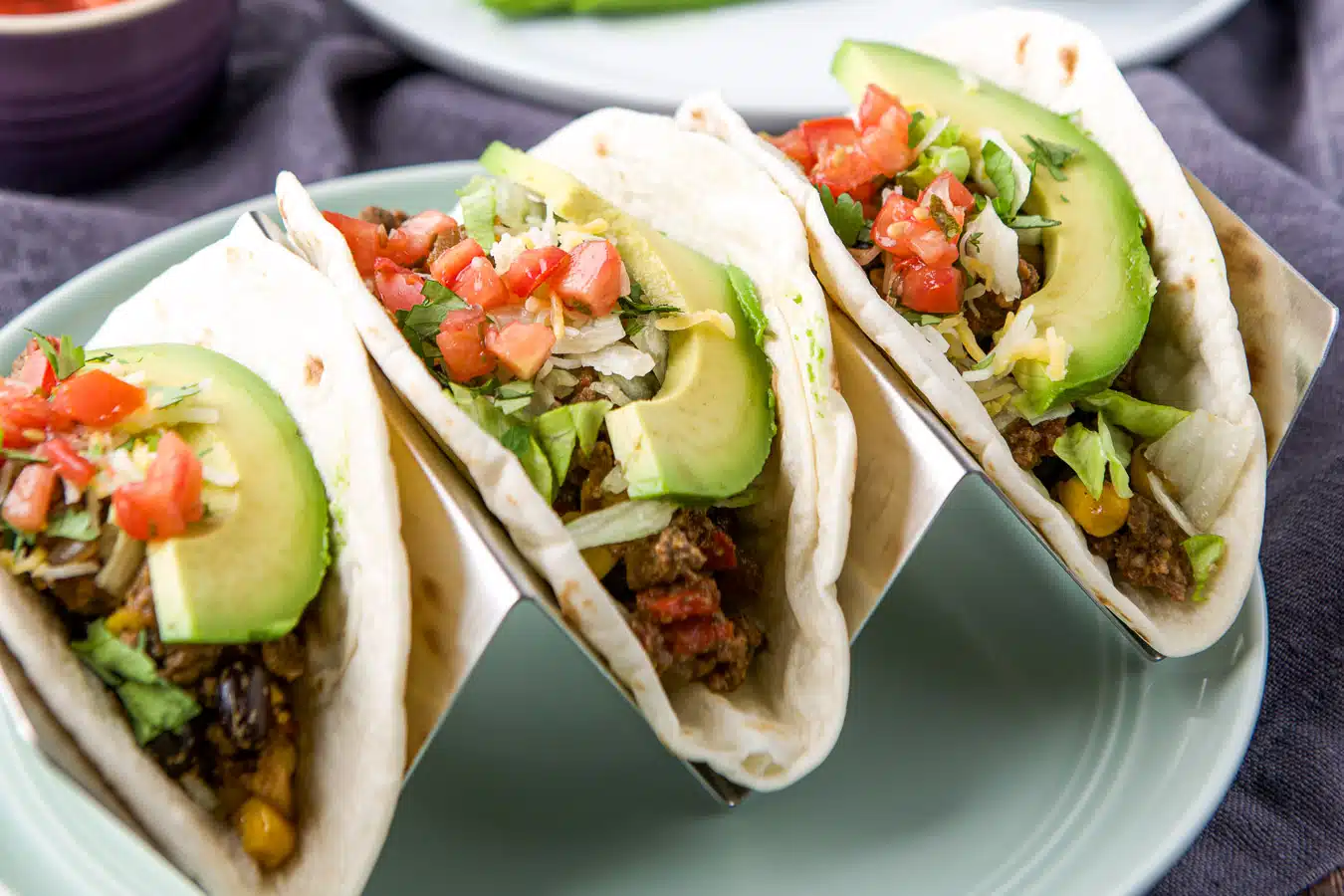 Horizontal photo of three soft tacos in a holder with all the ingredients on it