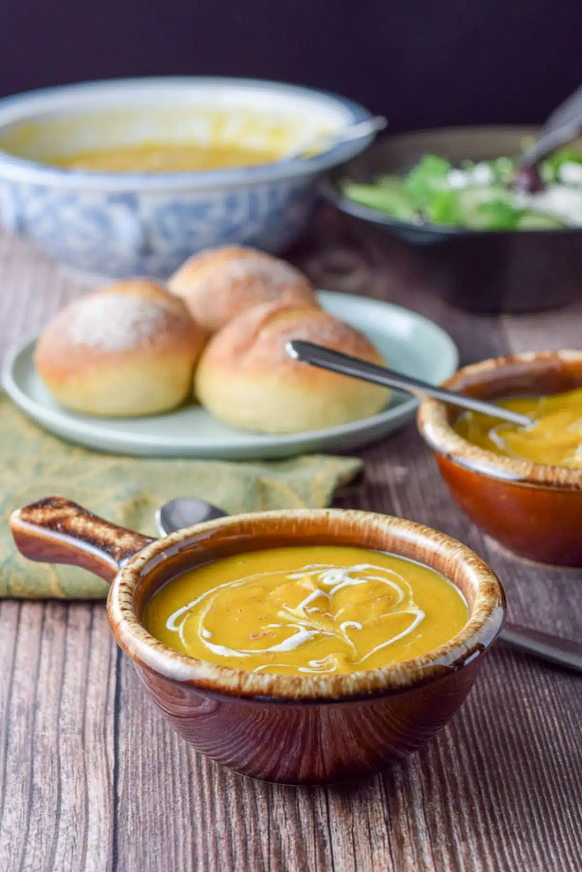 two bowls of squash soup with rolls in the background