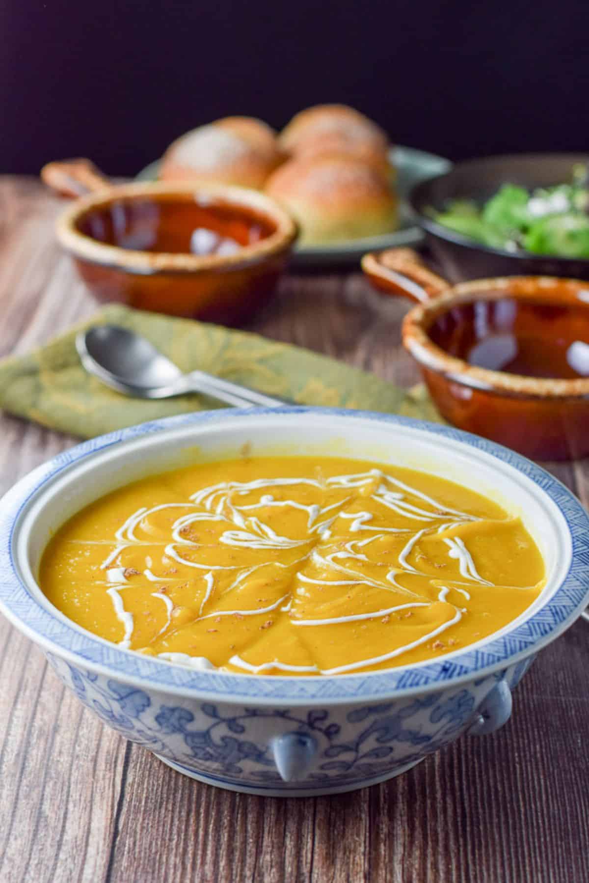 Sour cream squiggled on the thick squash soup with crocks and rolls in the background