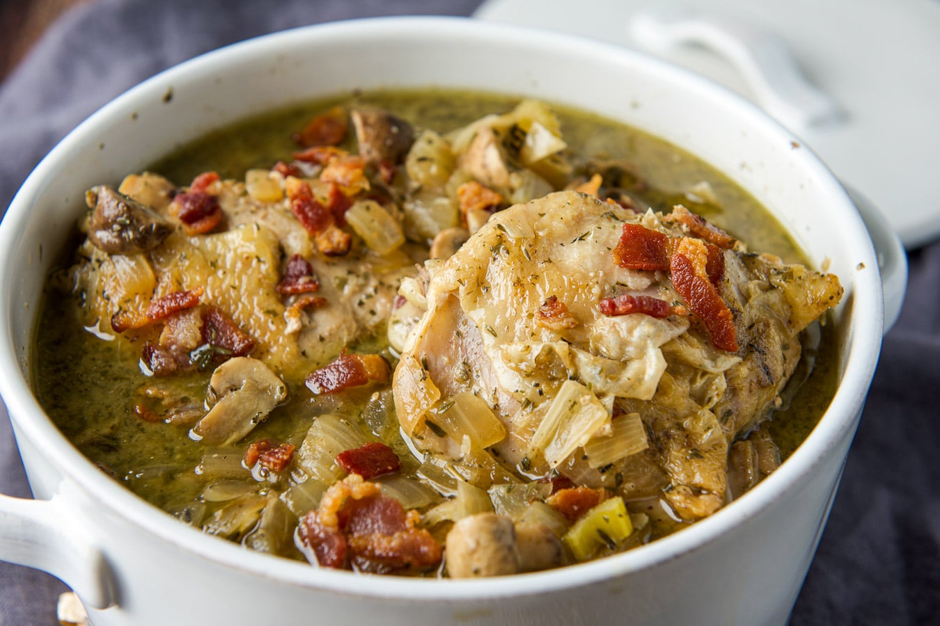 A white casserole dish filled with the coq au vin with bacon on top - horizontal