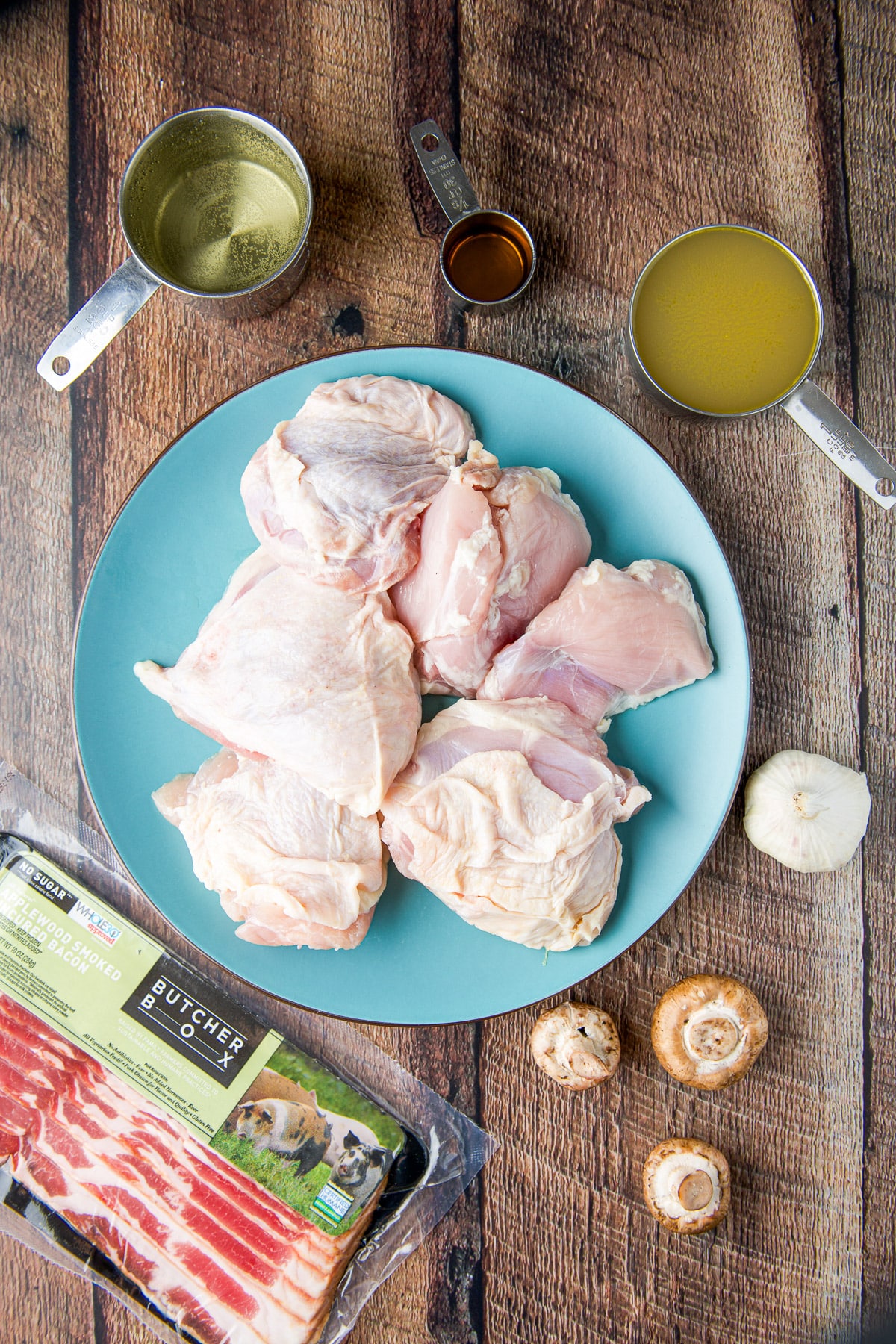 Overhead view of the ingredients - chicken thighs, bacon, broth, white wine, cognac, garlic, and mushrooms
