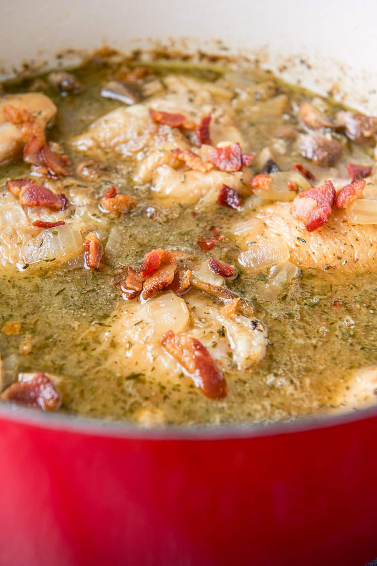 A close up of a red pan with chicken, bacon, and broth