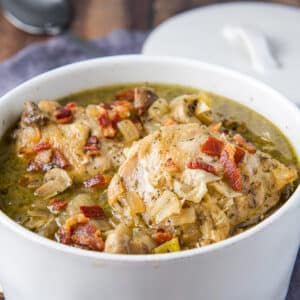 A square photo of chicken, broth, vegetables and broth in a white pan