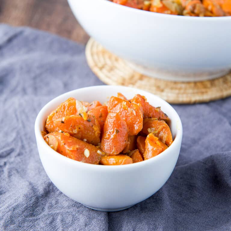square photo of a small white bowl filled with cooked carrots and onion