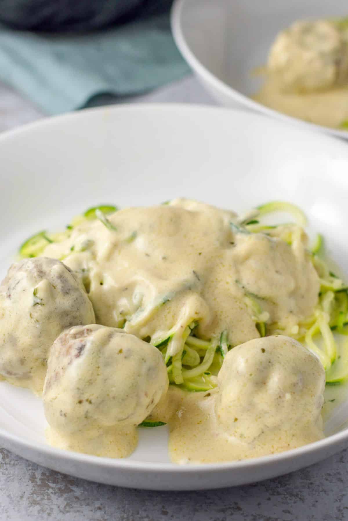 A close up view of a deep dish of Swedish meatballs with sour cream sauce on zoodles