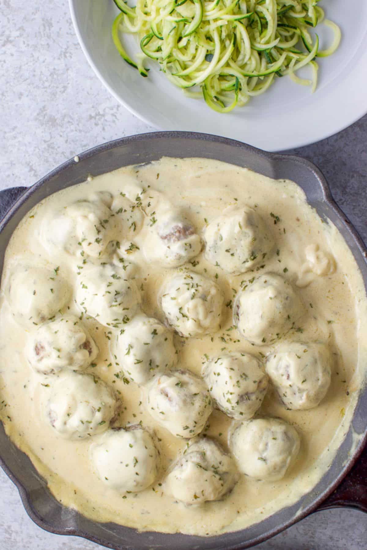 Overhead view of the pan of Swedish meatballs with sour cream sauce. There is also a plate of zoodles on the upper right