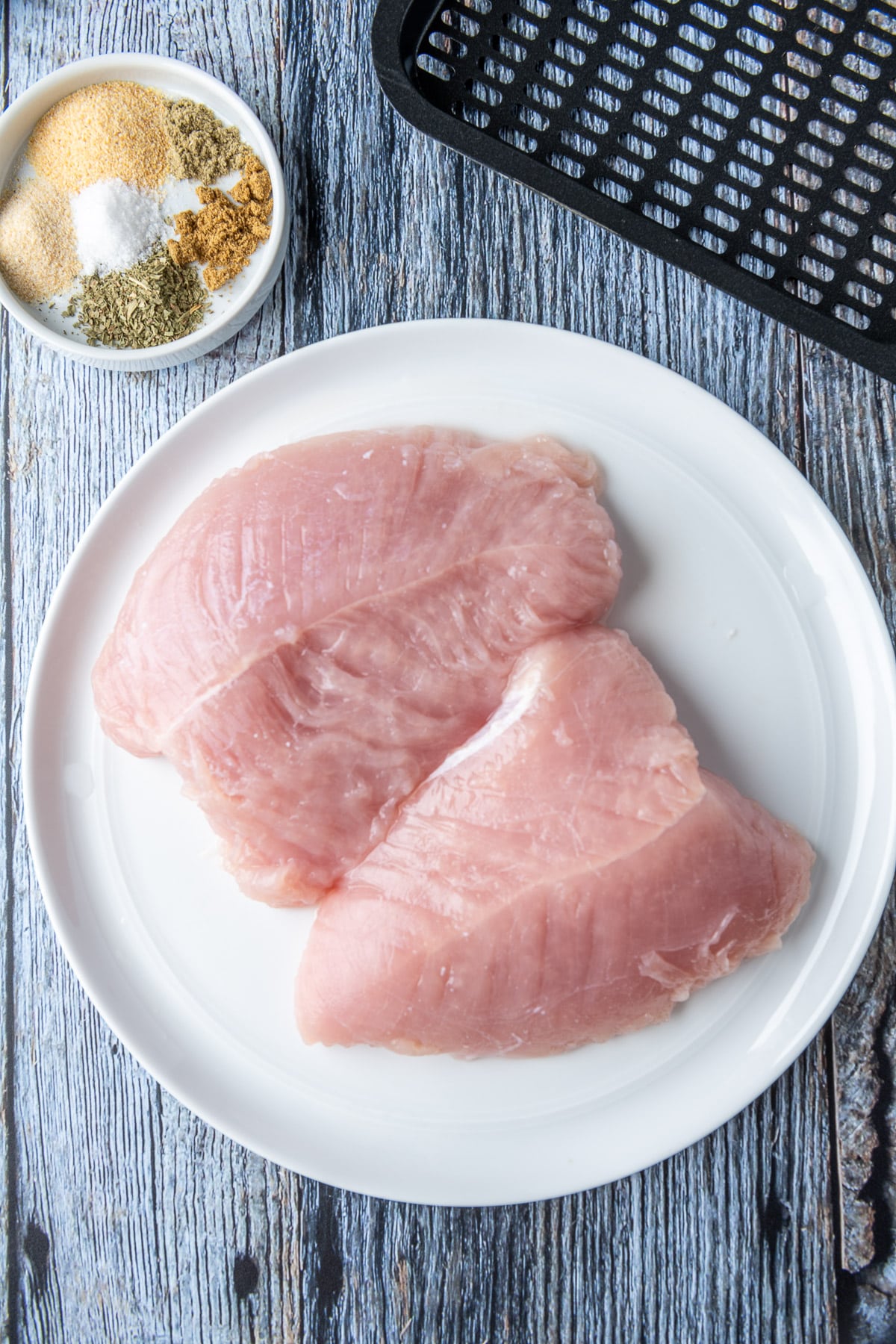 Overhead view of a white plate with raw turkey tenderloins and a small white plate with herbs and spices