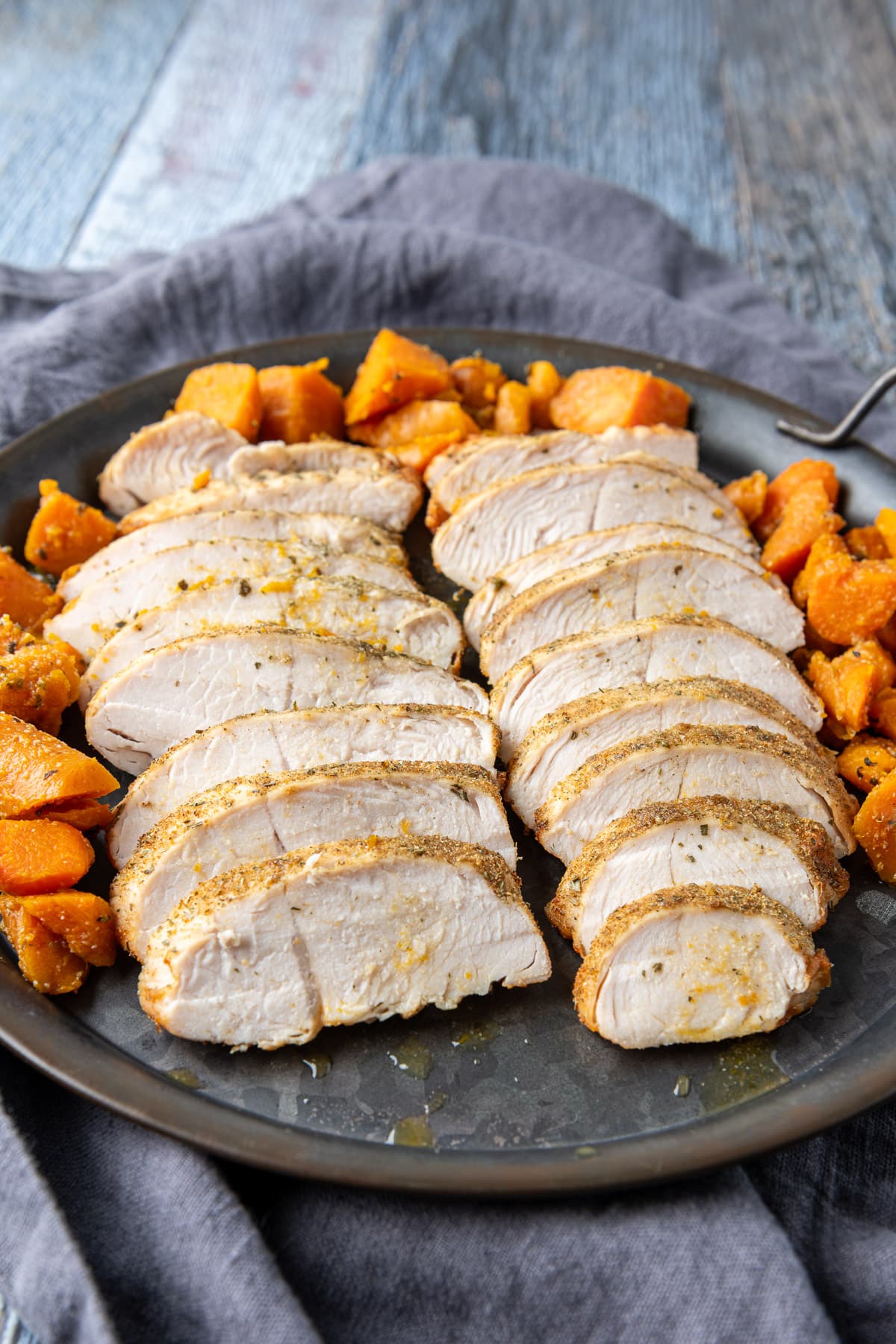 A grey napkin under a metal tray with carrots and sliced turkey tenderloin